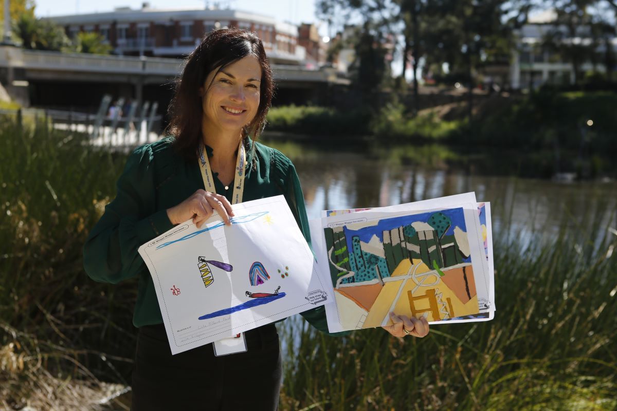A woman stands outside near the Wollundry Lagoon in Wagga Wagga holding some artworks on paper. 