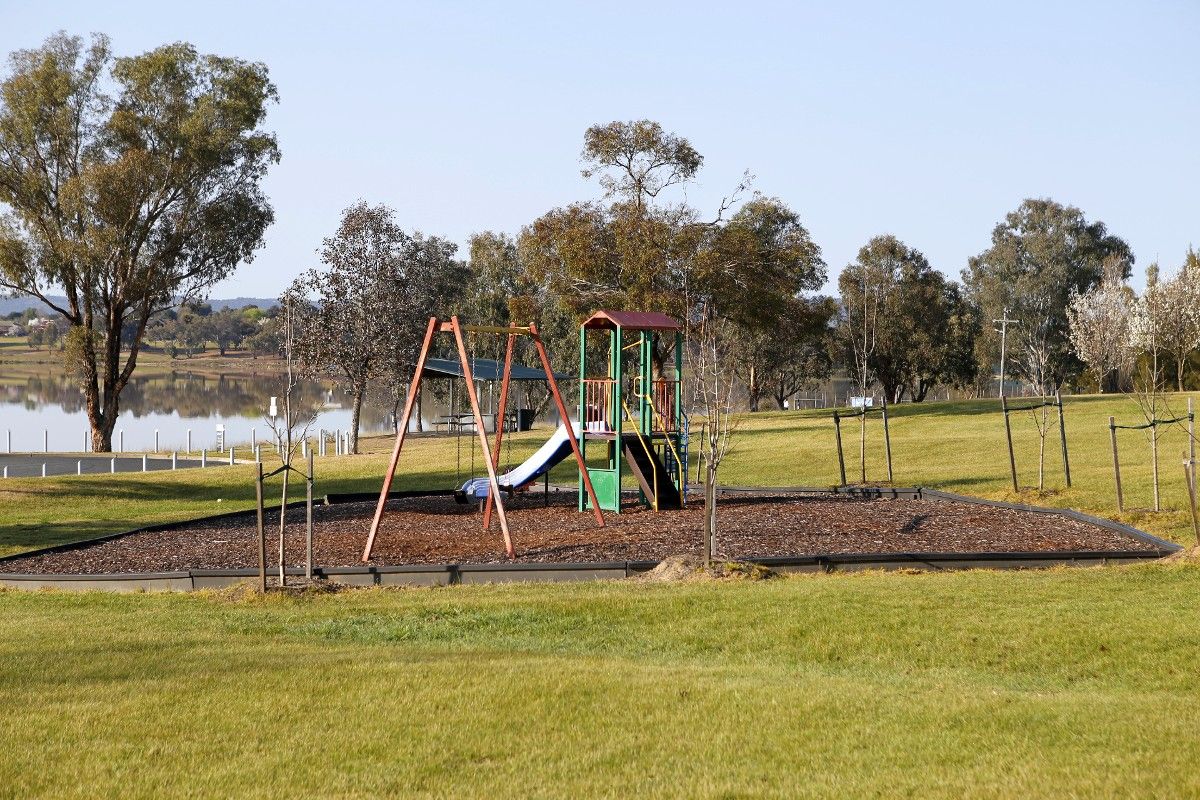 Playground equipment including swings, slippery slide and climbing tower, surrounded by soft fall bark chips, located inside a grassy area of a park.