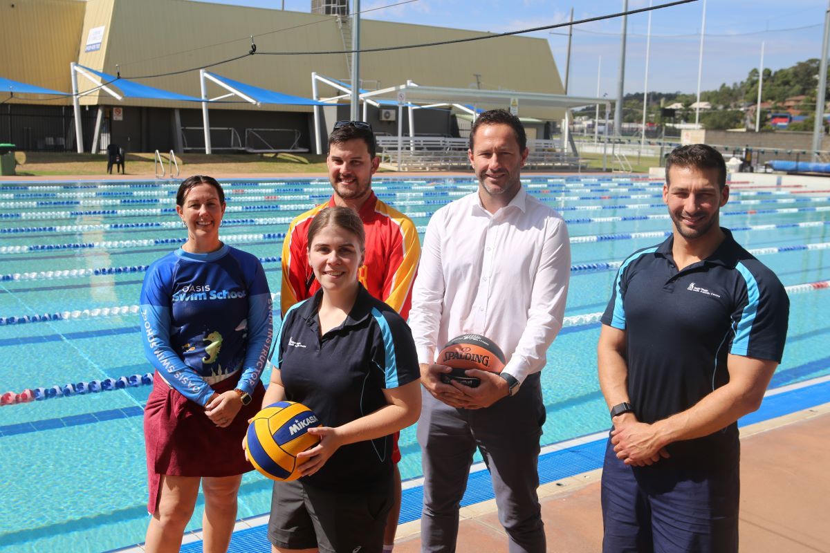 A group of three men and two women standing beside an outdoor lane pool. 