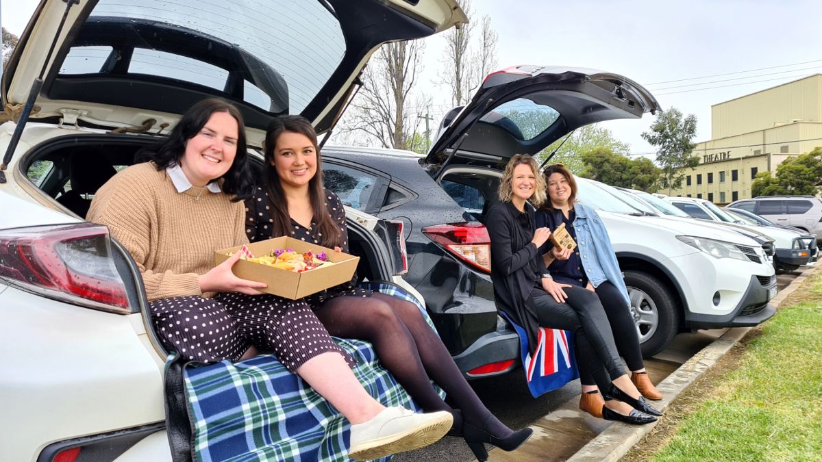 Four women sitting in back of SUVs, holding food
