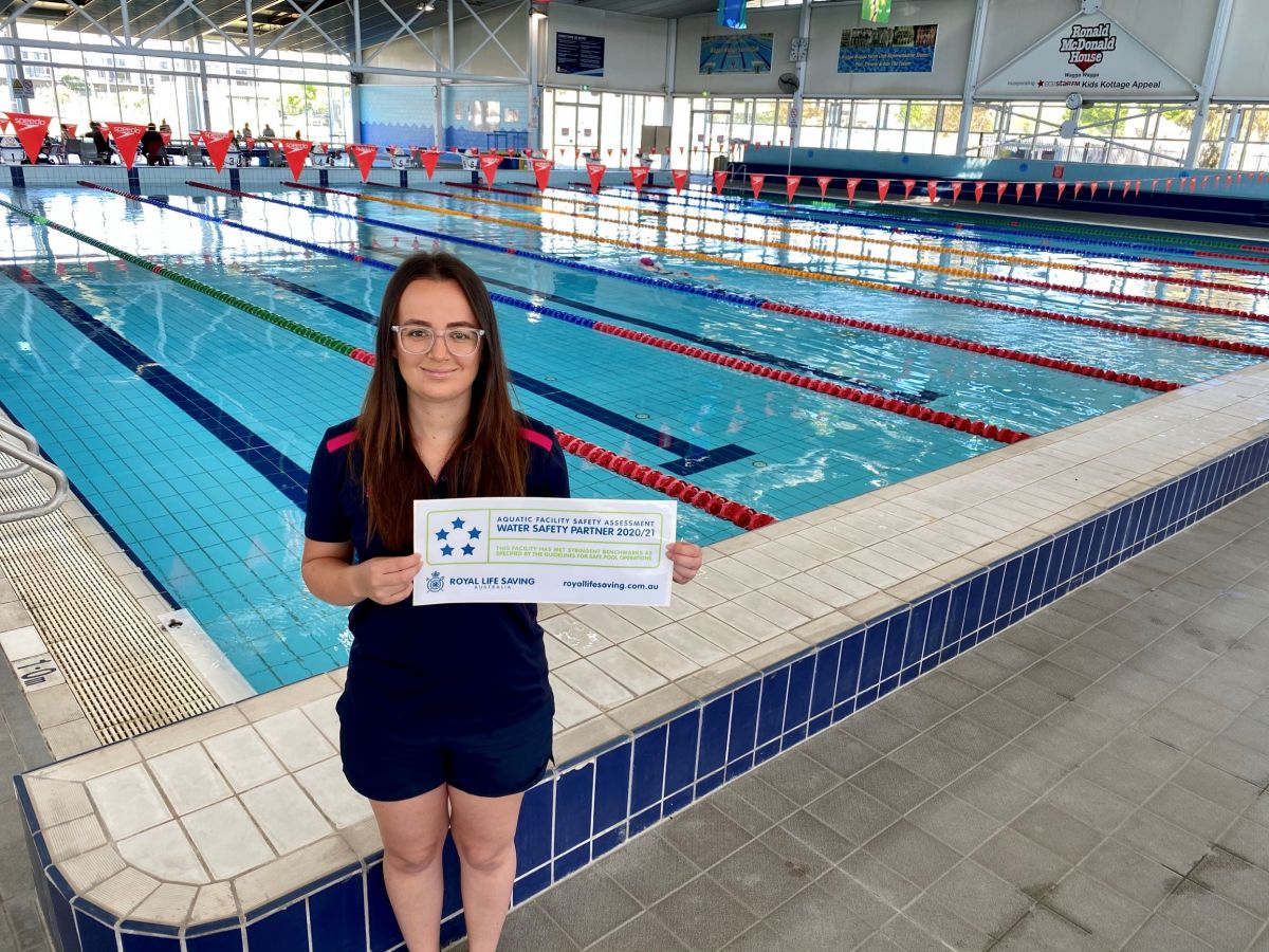 Young woman standing in front of pool holding a water safety partner sign