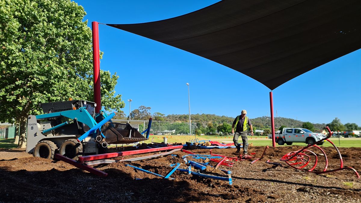 Bobcat clearing equipment from playground with man standing under shade sail