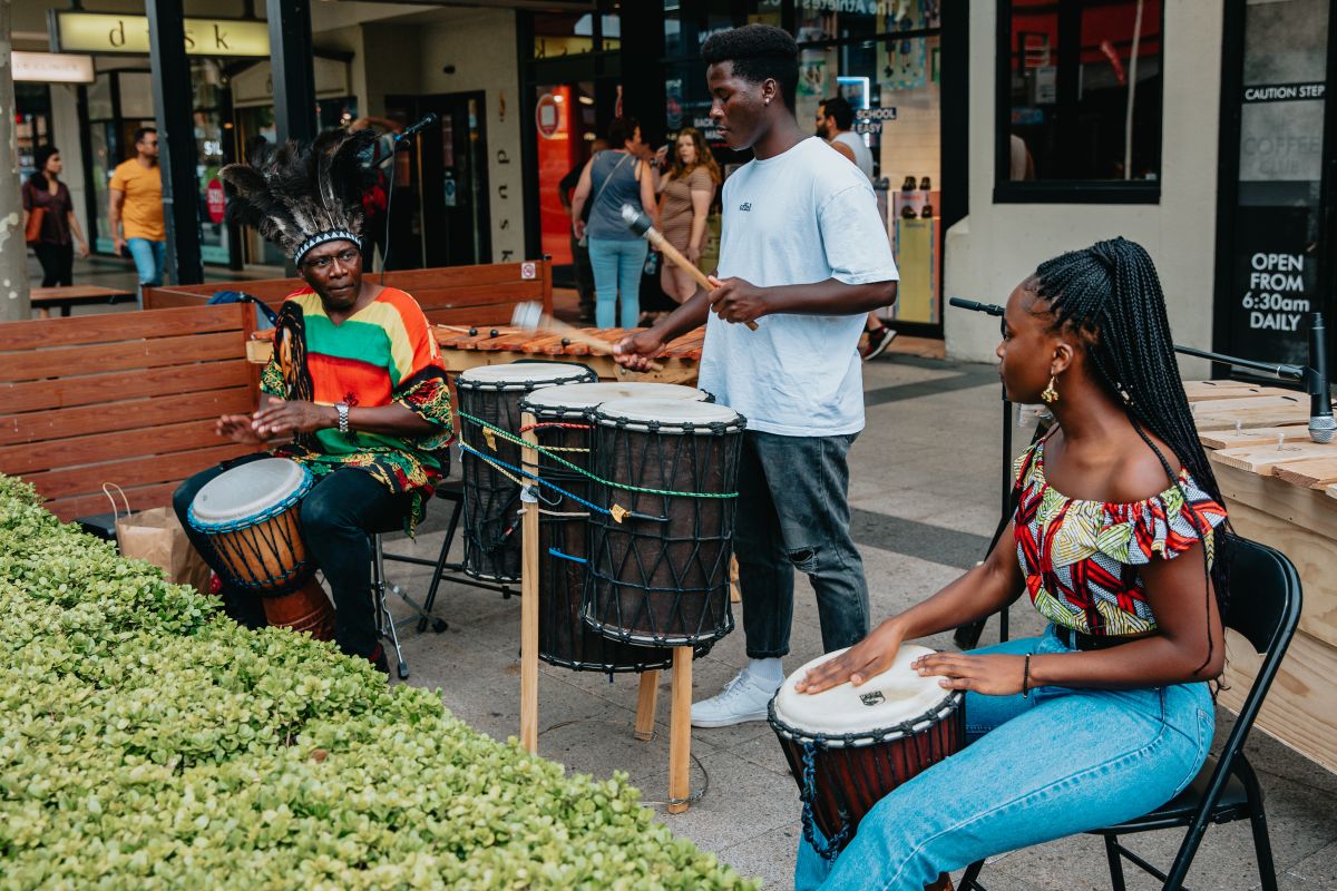 Two men and a woman playing bongo drums on the footpath in CBD area