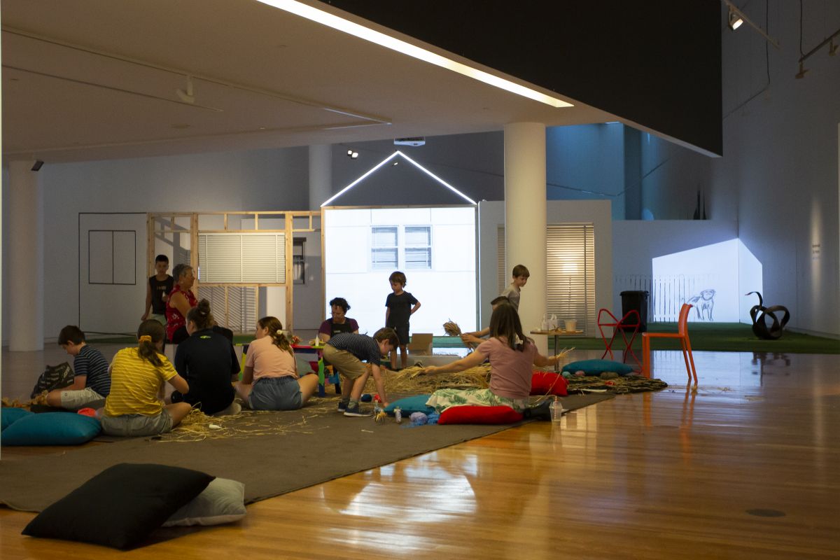 children and adults sitting on cushions and floor creating raffia pets