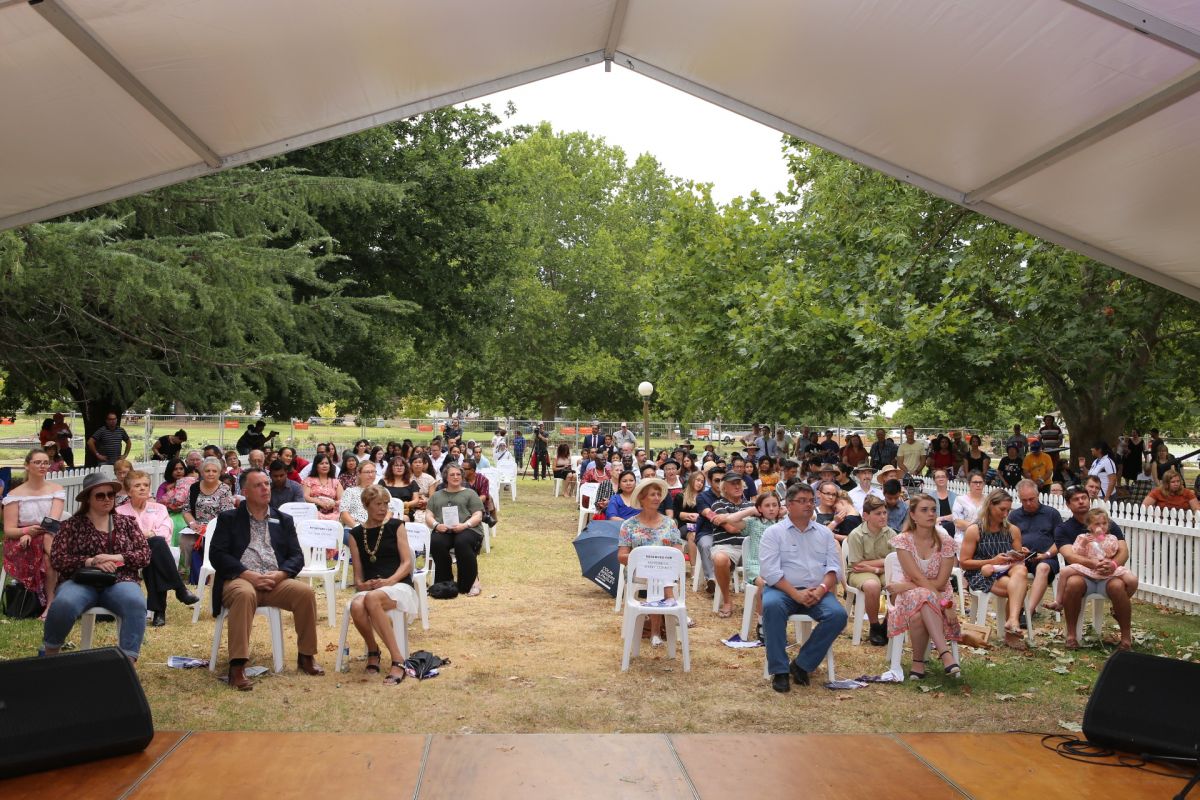 Crowd seated on chairs on grass in front of marquee