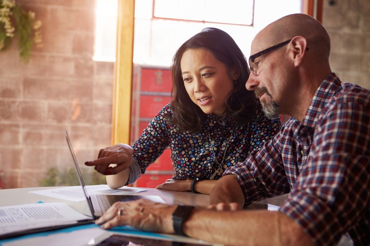 A woman and man sitting at a desk looking at a laptop