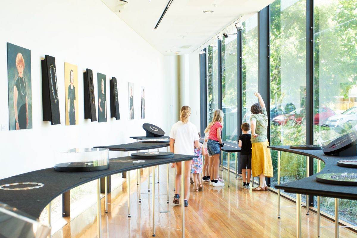 Jewellery art work on wall and young children in background looking at exhibits