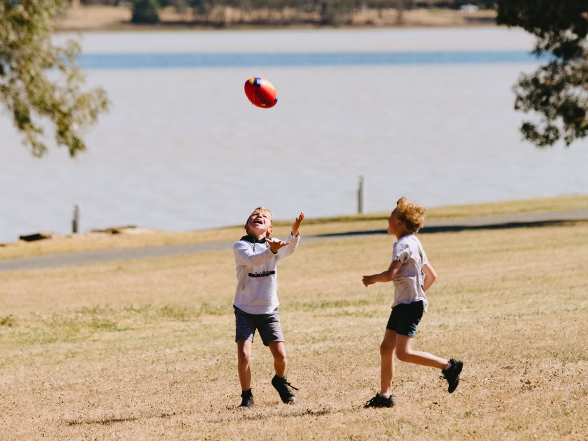 Two boys playing football beside a lake
