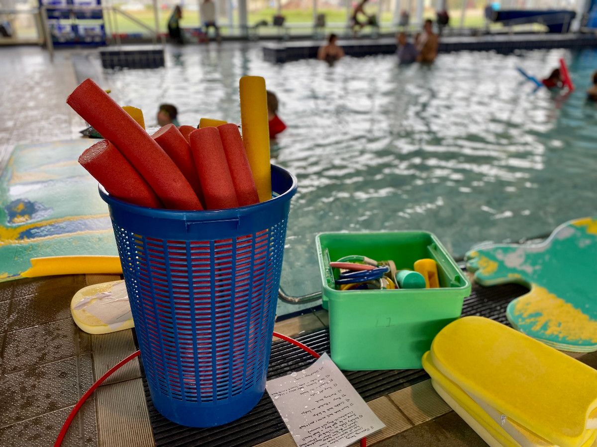 Pool noodles in a basket beside a pool