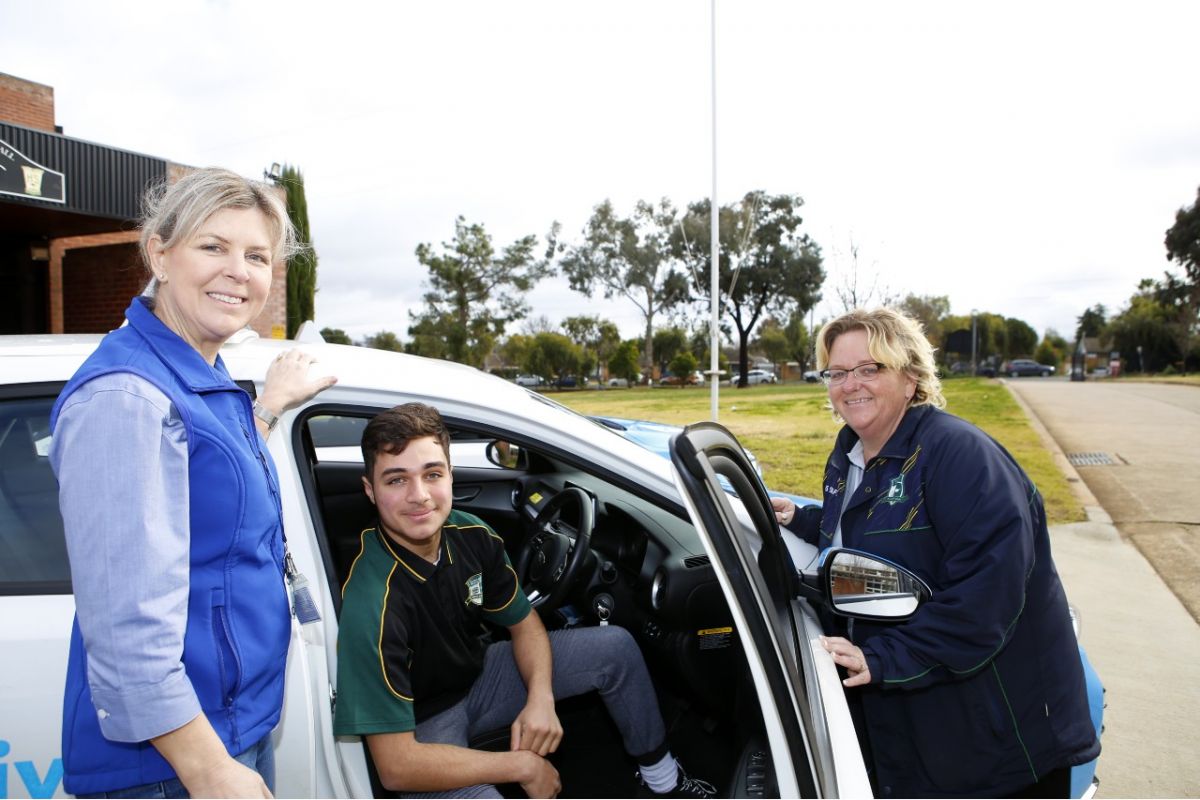 Female driving instructors, male high school student sitting in car, female school principal beside car
