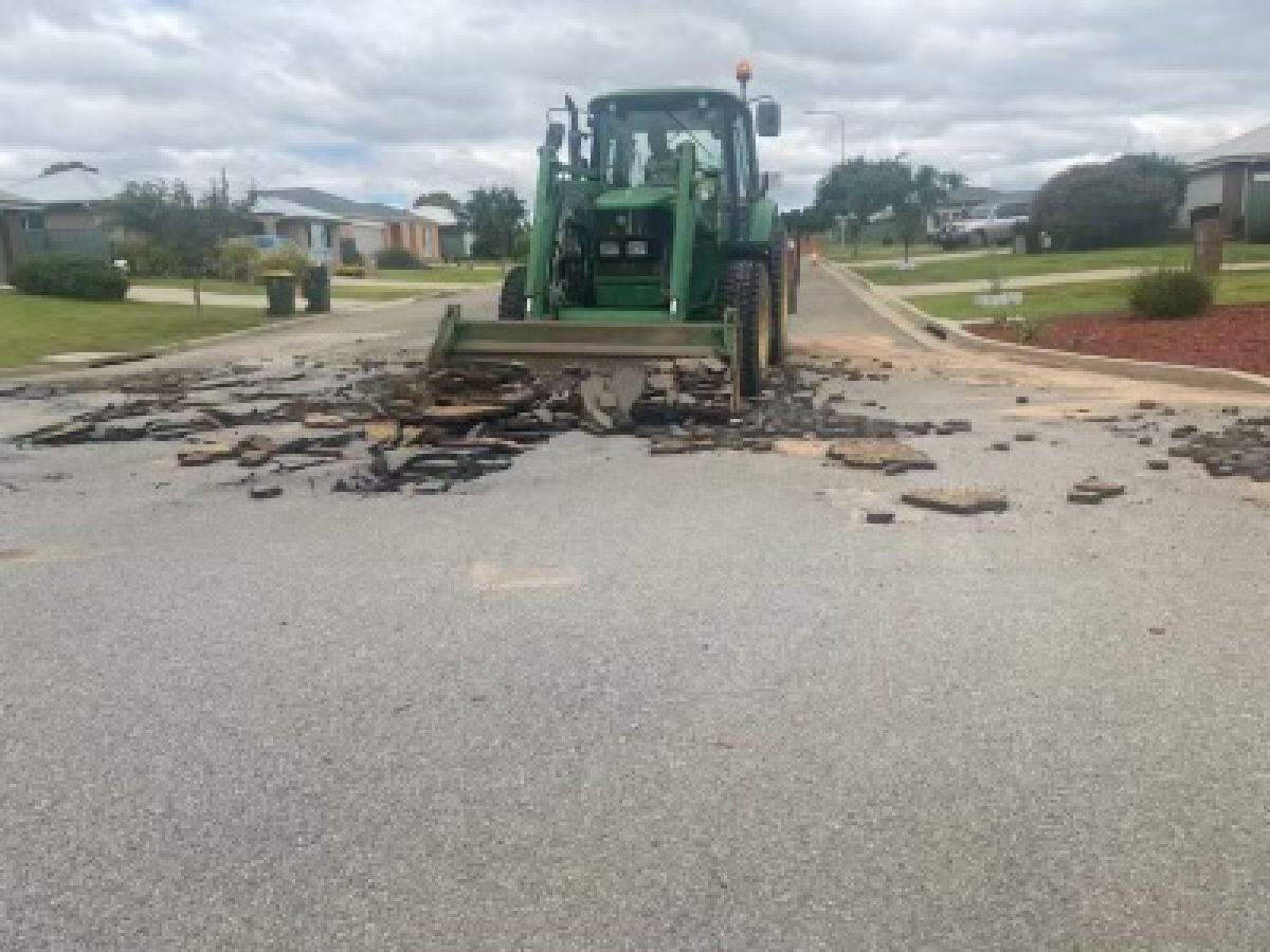 A green tractor scoops up broken bitumen from a road surface