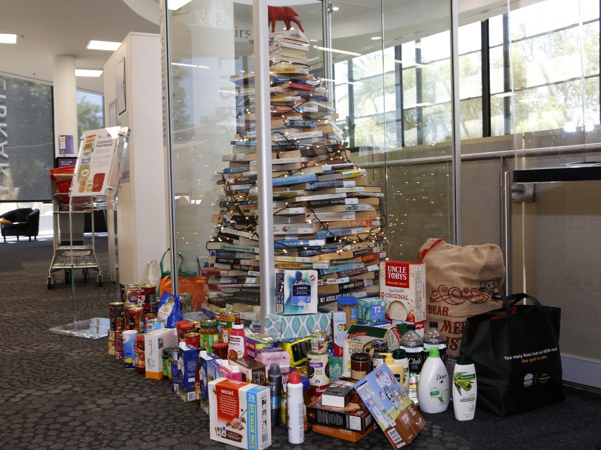 non perishable food items piled around christmas tree made out of books
