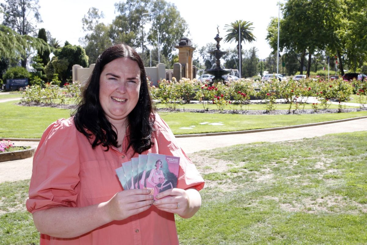 Woman holding copies of a guide, with garden and fountain in background