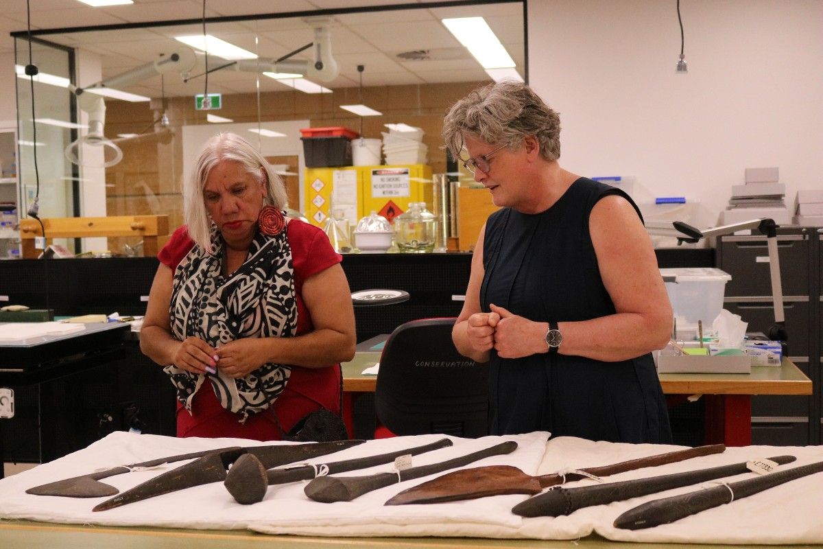 Wiradjuri elder and another female looking at seven Wiradyuri objects on a table