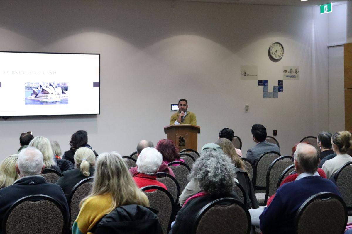 Emcee Ali Hamza speaks to the audience at Refugee Week event 2023.