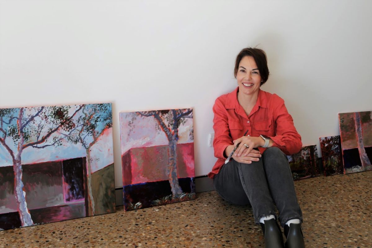 a woman sitting on the floor amongst her paintings