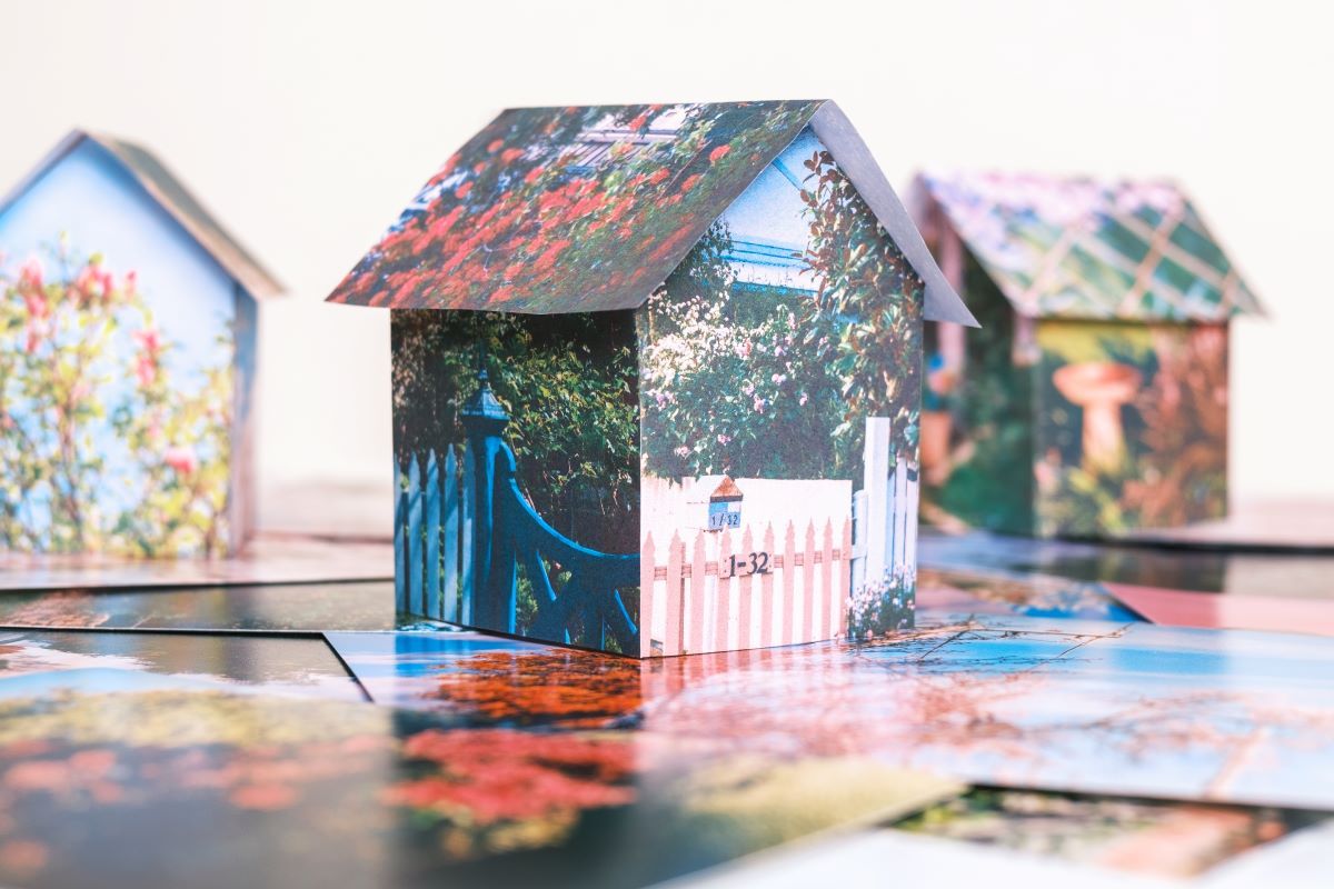 a small structure shaped like a house made of photographs. It is sitting on some similar photographs. 