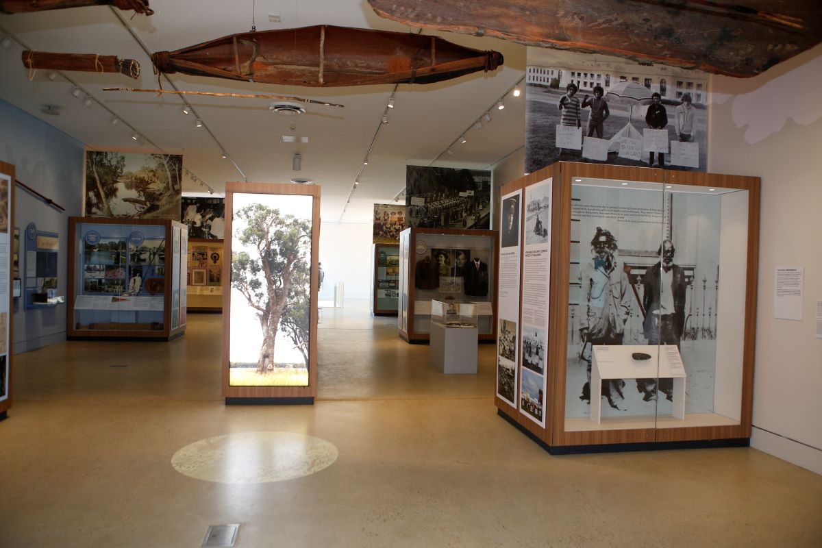 The interior of a museum with wooden artefacts hanging from the ceiling, display cases and large photographs. 