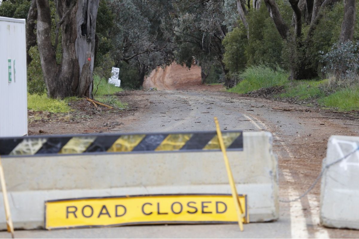 Road closed sign leaning against cement barriers with road in background