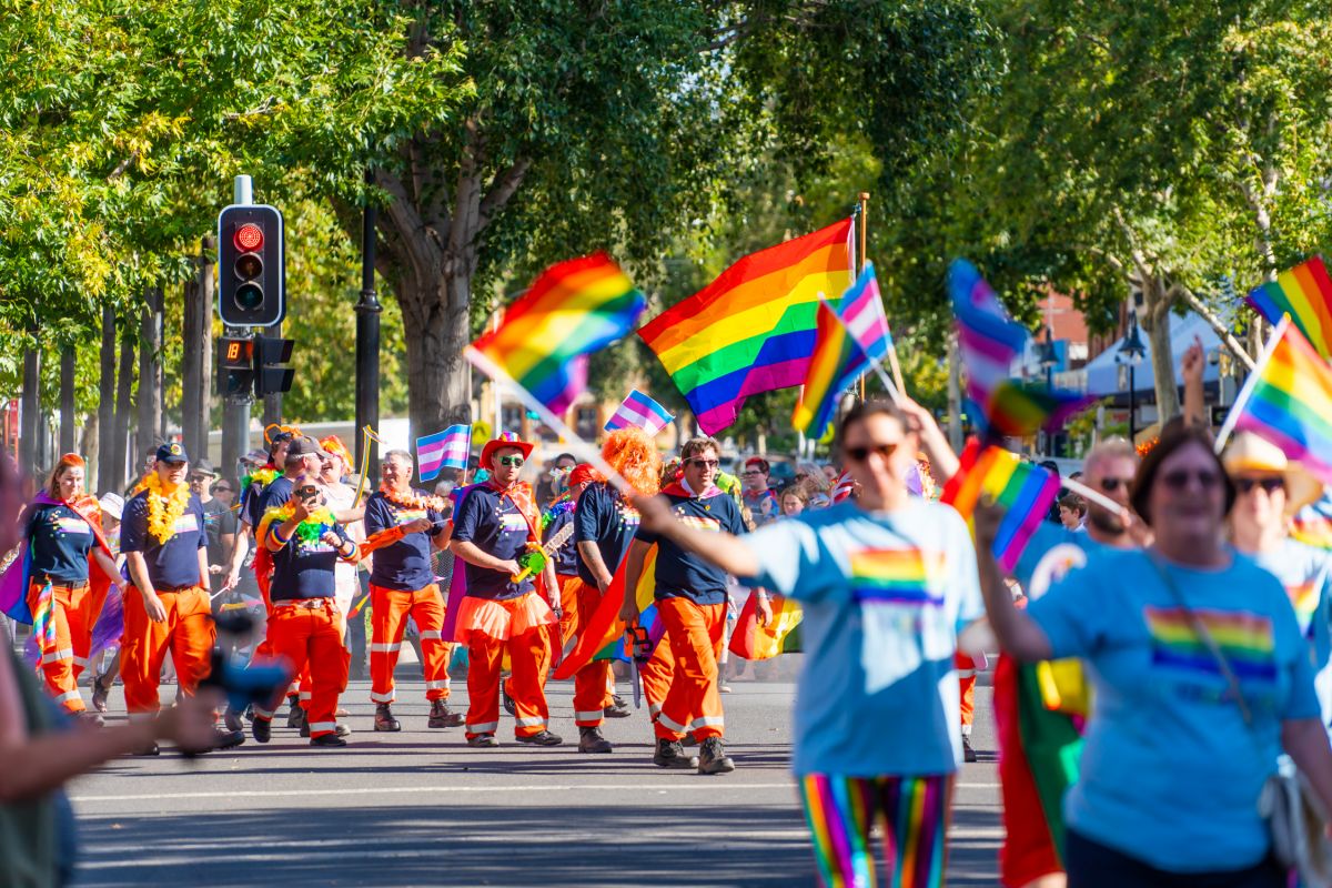 Wide shot of Mardi Gras parade as people walk and wave flags down Baylis Street in Wagga Wagga.