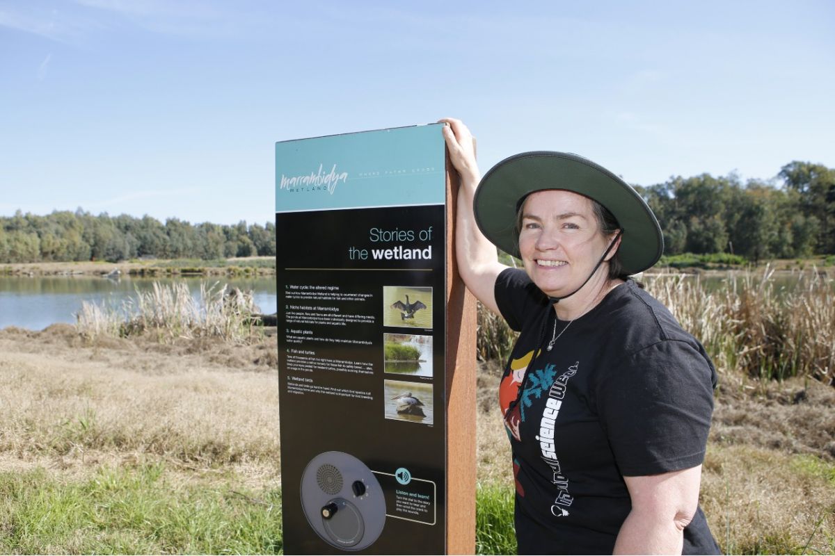 Woman standing beside sign for Marrambidya Wetland with pond in background