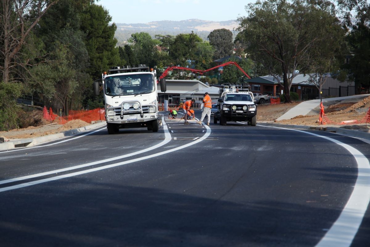 Trucks and contractors apply white lines and markings on a new road surface.
