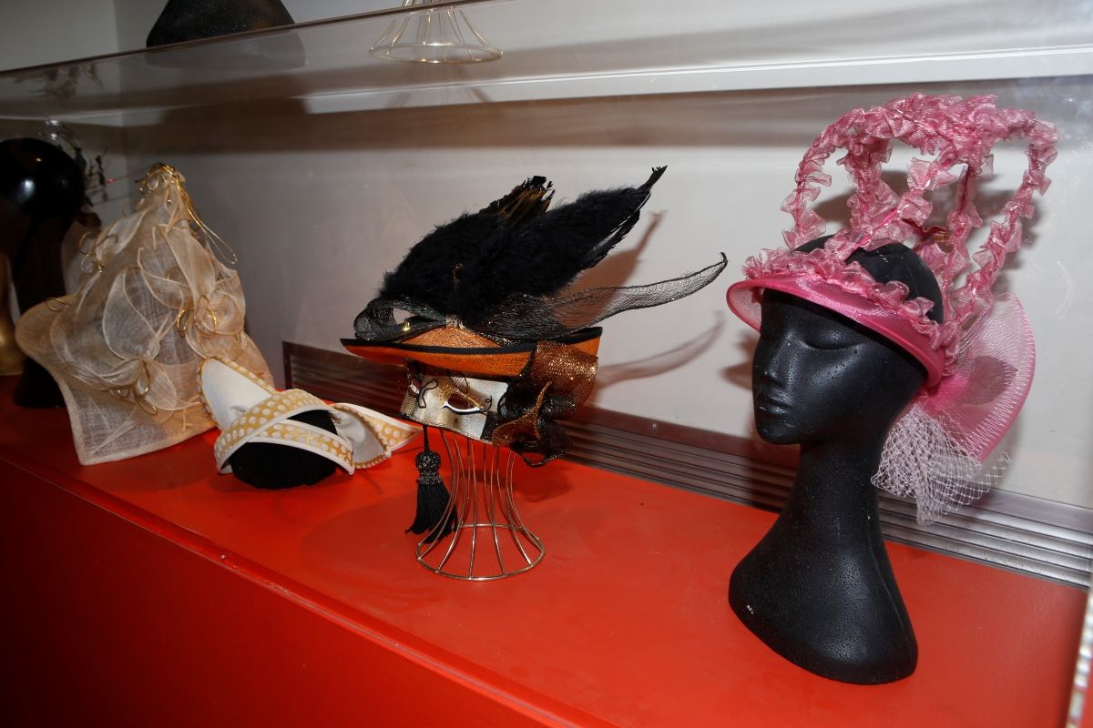 Several hand-made hats sitting in a glass display cabinet.