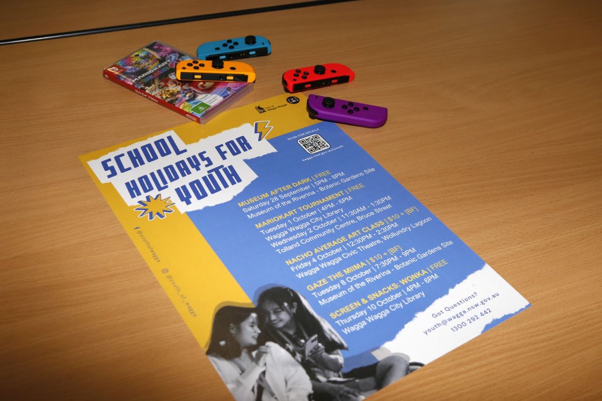 poster for the School Holidays for Youth program on desk with Mario Kart controllers nearby