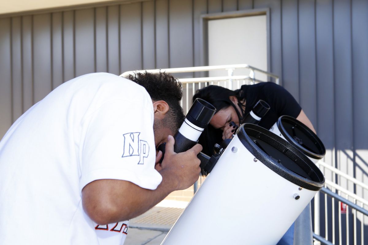 A man and a woman looking through the view finder on white telescopes.