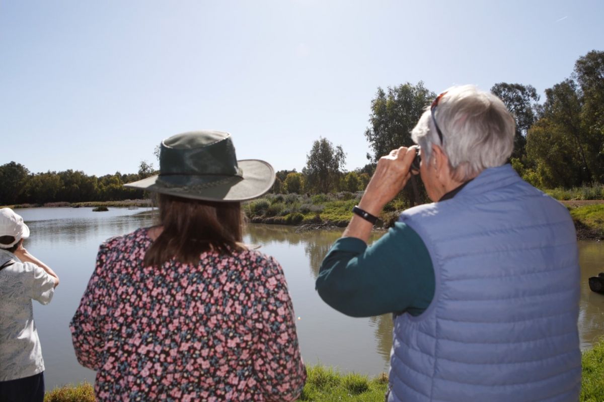 People looking out towards a lake. One holds a pair of binoculars.