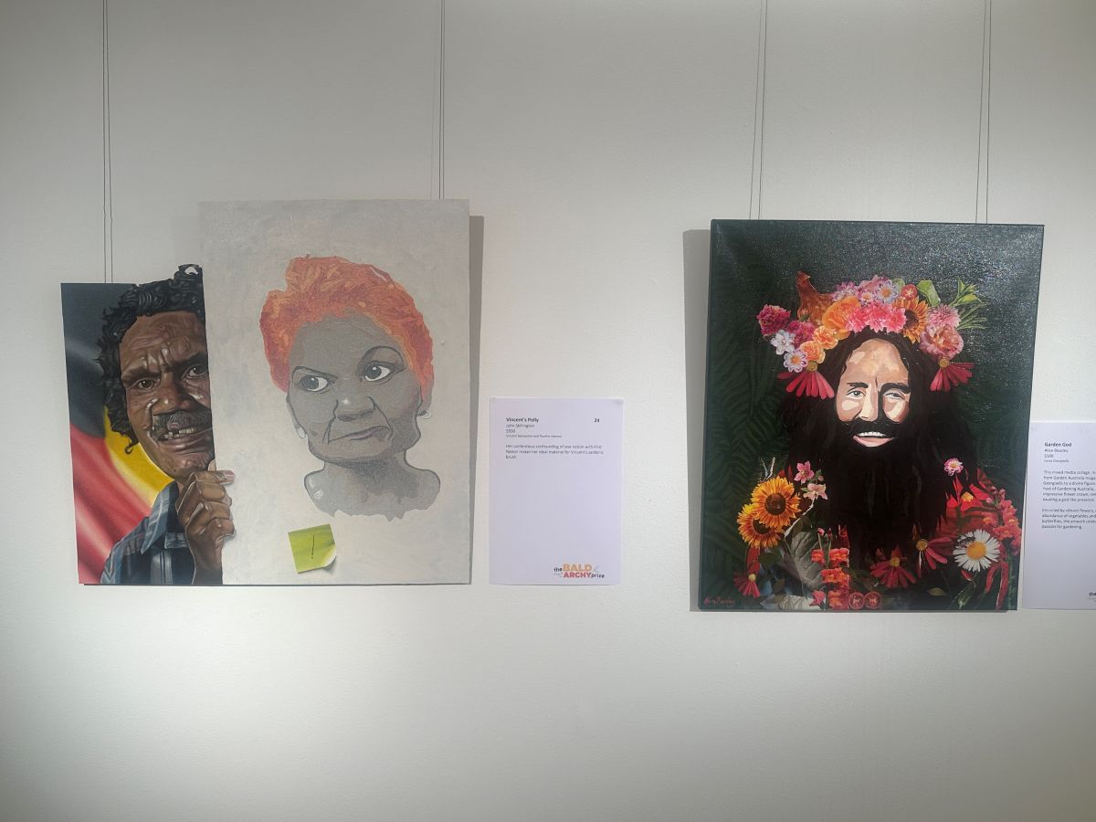 Two portraits hung on a gallery wall, one featuring a smiling First Nations activist Vincent Lingiari, with the Aboriginal Flag in the background, holding a portrait of Pauline Hanson, and the other of Costa Georgiadis from Gardening Australia, wearing a garland of flowers and a headpiece made of flowers.