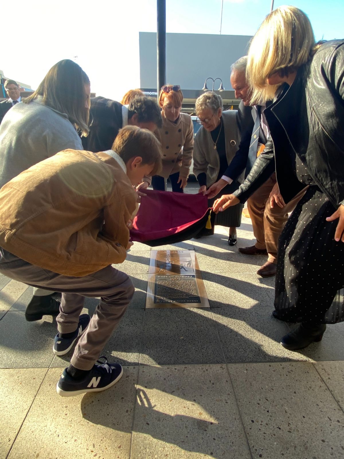 Women and men lifting covering from plaque on footpath