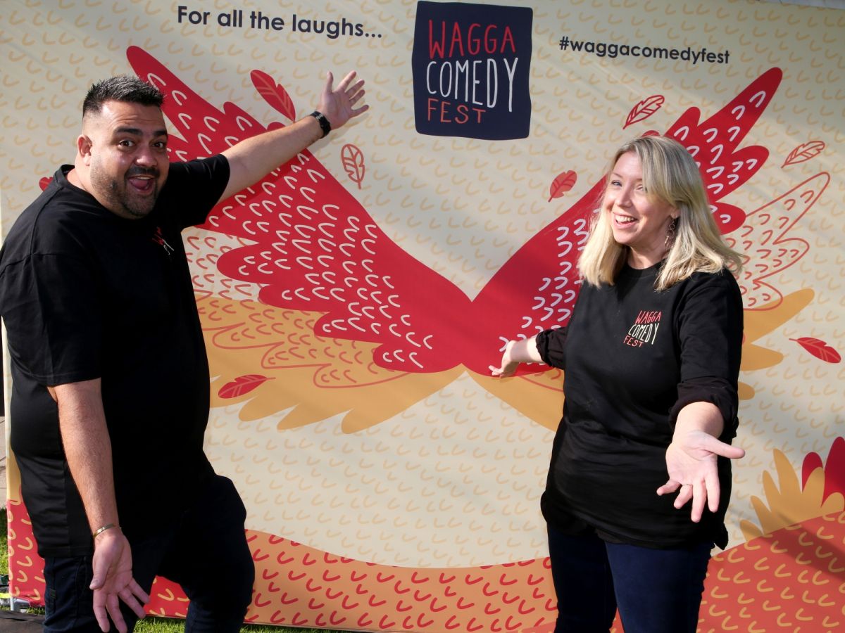 Man and woman laughing, standing in front of sign for Wagga Comedy Fest