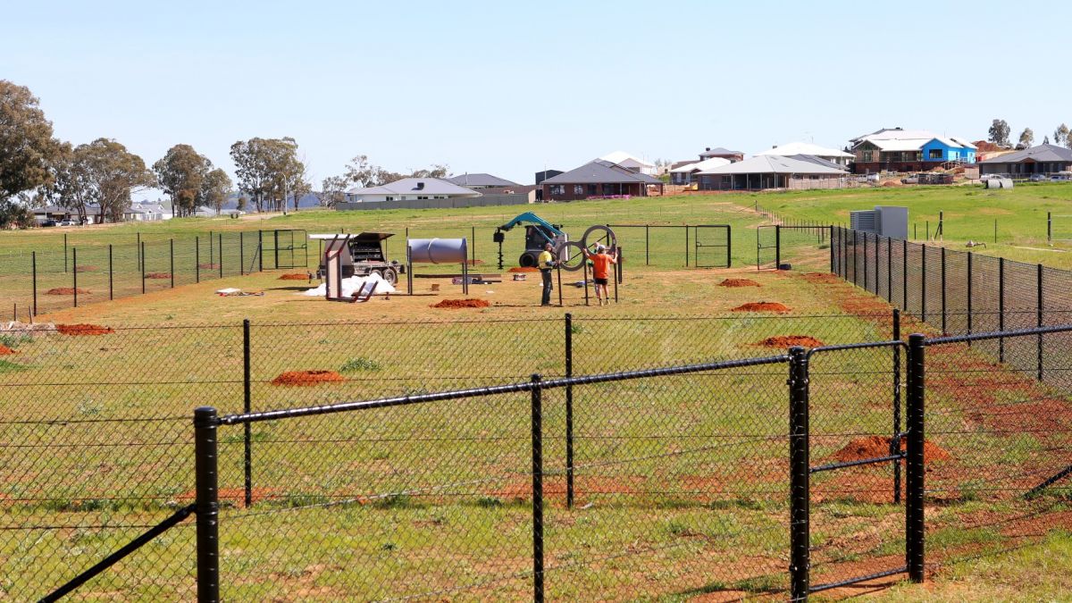 Fenced off-leash dog park with agility equipment in background