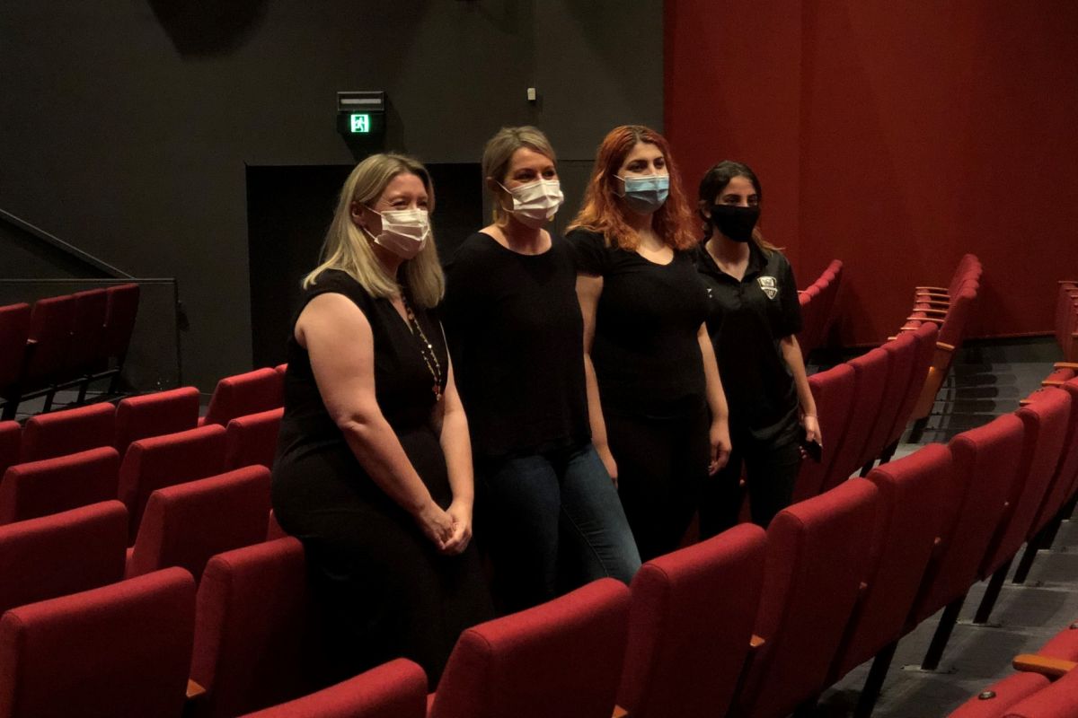 Four women standing side-by-side between row of theatre seats