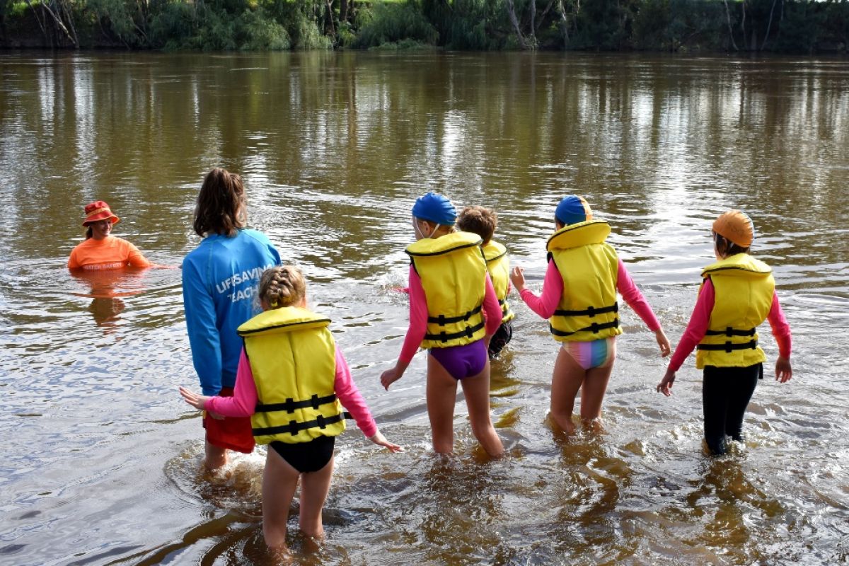Children wade into river with swimming teacher watching
