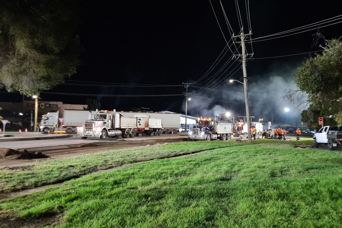 Wide shot of road rehabilitation works at night with trucks & machines
