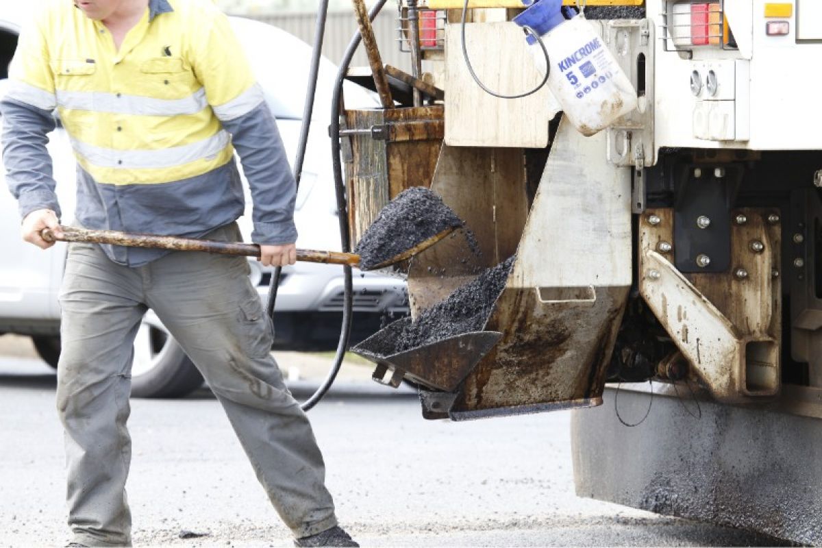 A man lifts a shovel load of bitumen from a truck