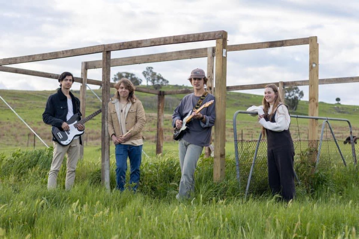 Three young men and a young woman stand in a grassy paddock