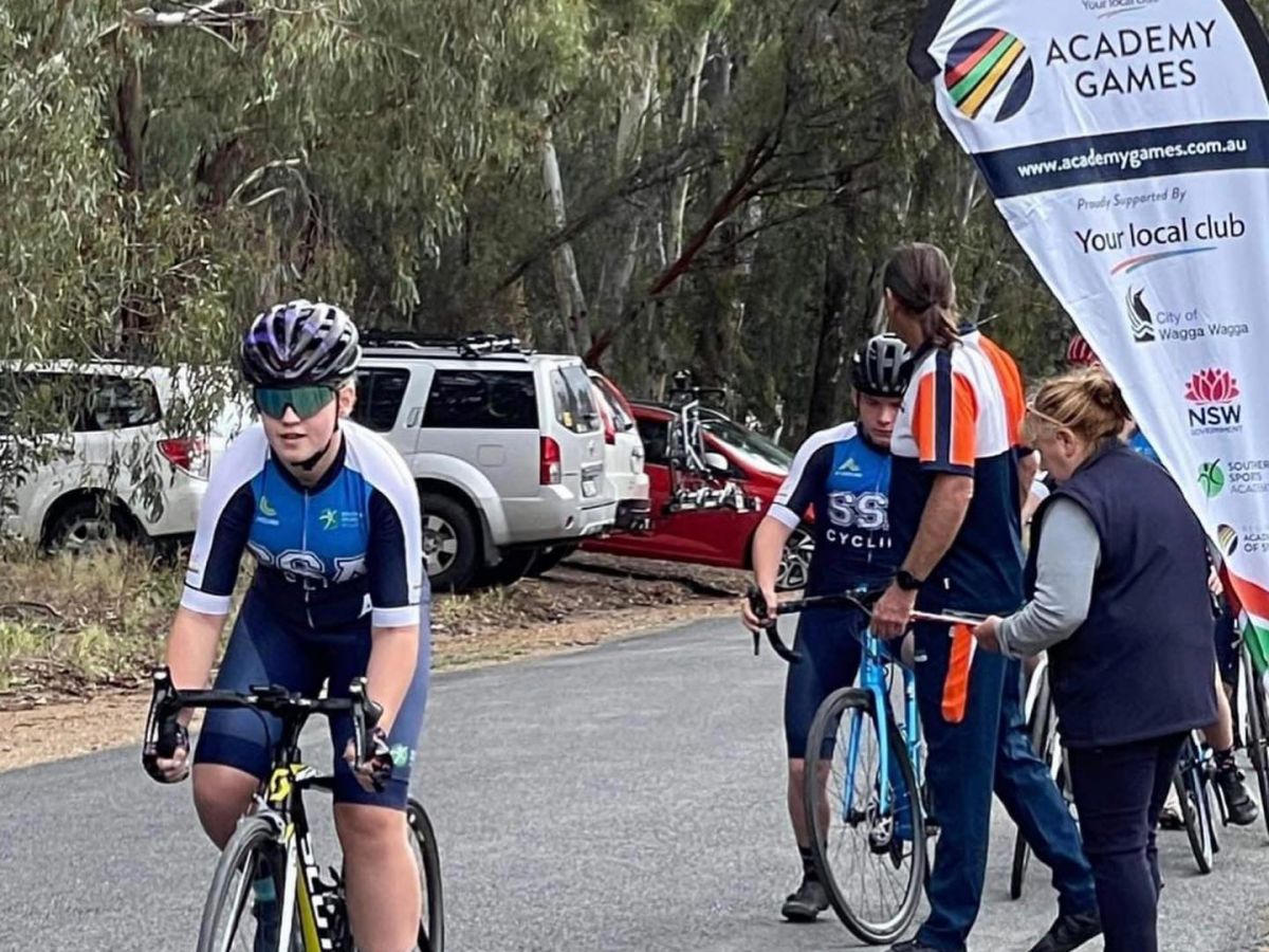 Young boy on road racing bike with other riders and adults in background