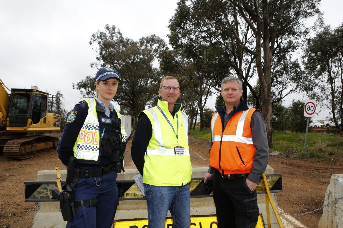 Female Highway Patrol officer and two men in hi-vis vests standing in front of a road closed sign leaning against concrete barriers