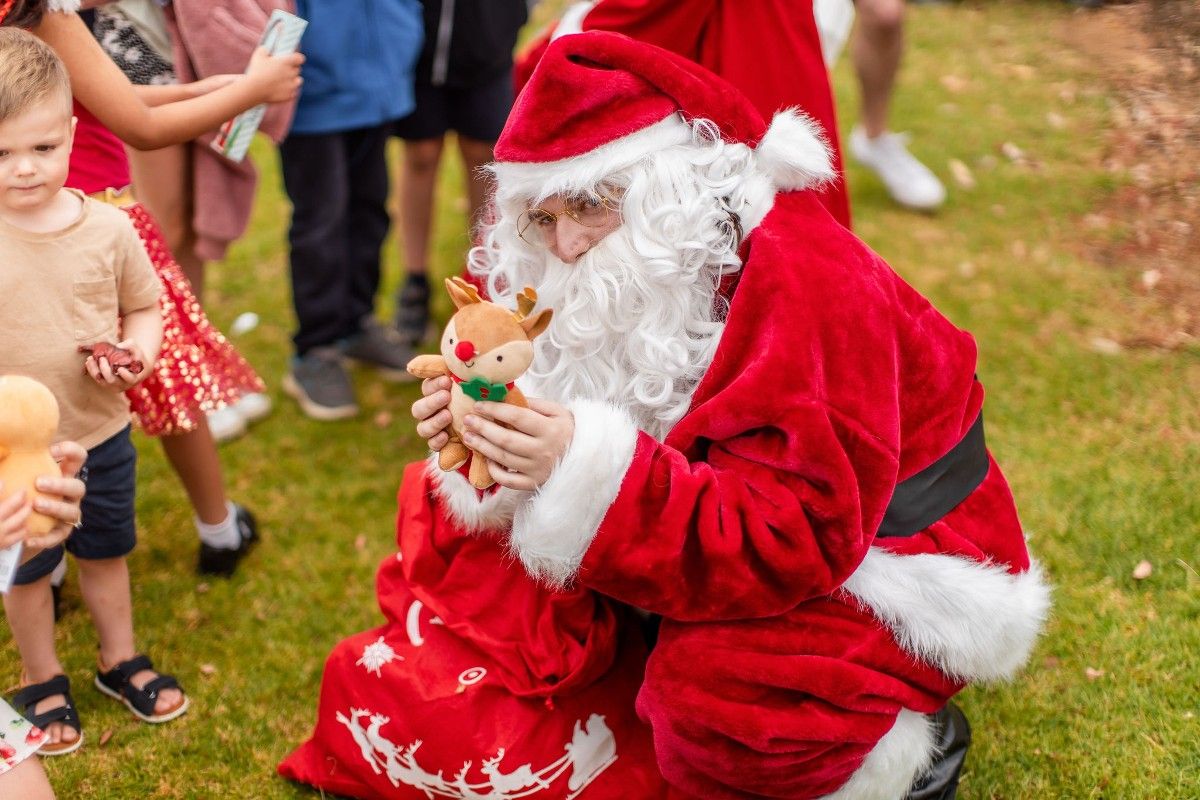 Man dressed as Santa with bag of gifts, with young children in background