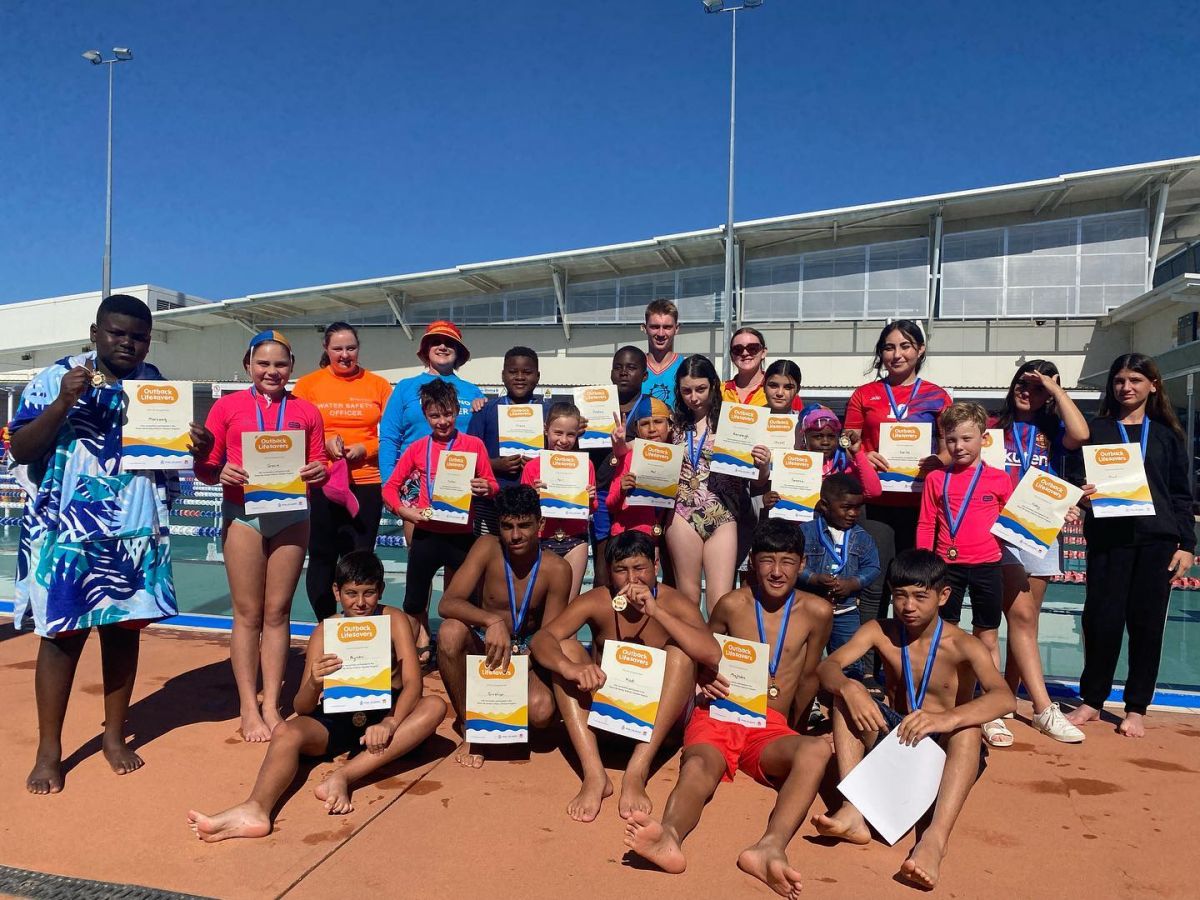 Group of young people in swimming gear holding up certificates, standing next to a pool