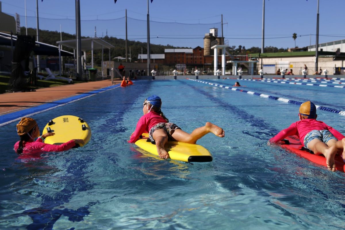 Rear view of three young people on rescue boards on outdoor 50-metre swimming pool
