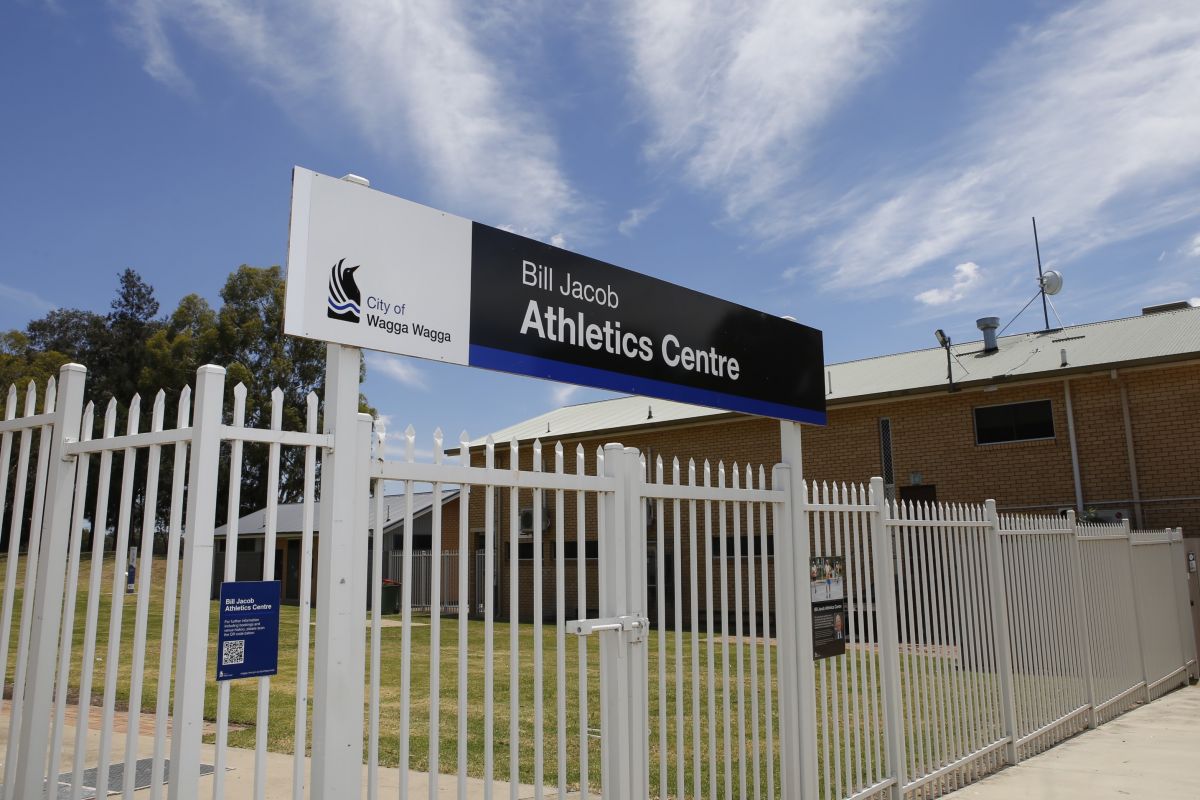 A sign is mighted on white fencing outside the Bill Jacob Athletics Centre, reading the name of the building and accompanied by the Wagga Wagga City Council logo.