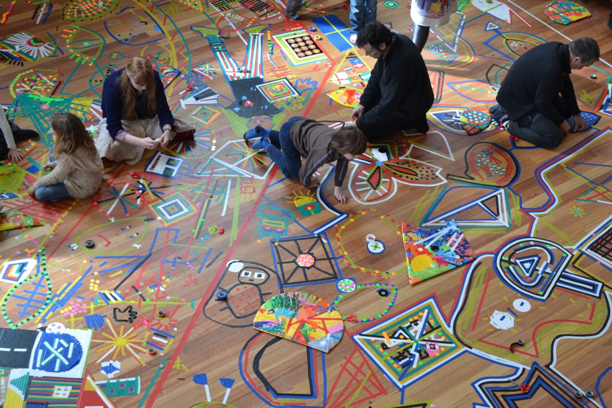People of all ages using tape to create artworks on a vinyl floor.