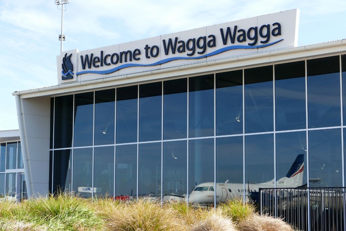 Airport terminal with Welcome to Wagga Wagga sign on roof and aircraft reflected in the glass windows. 