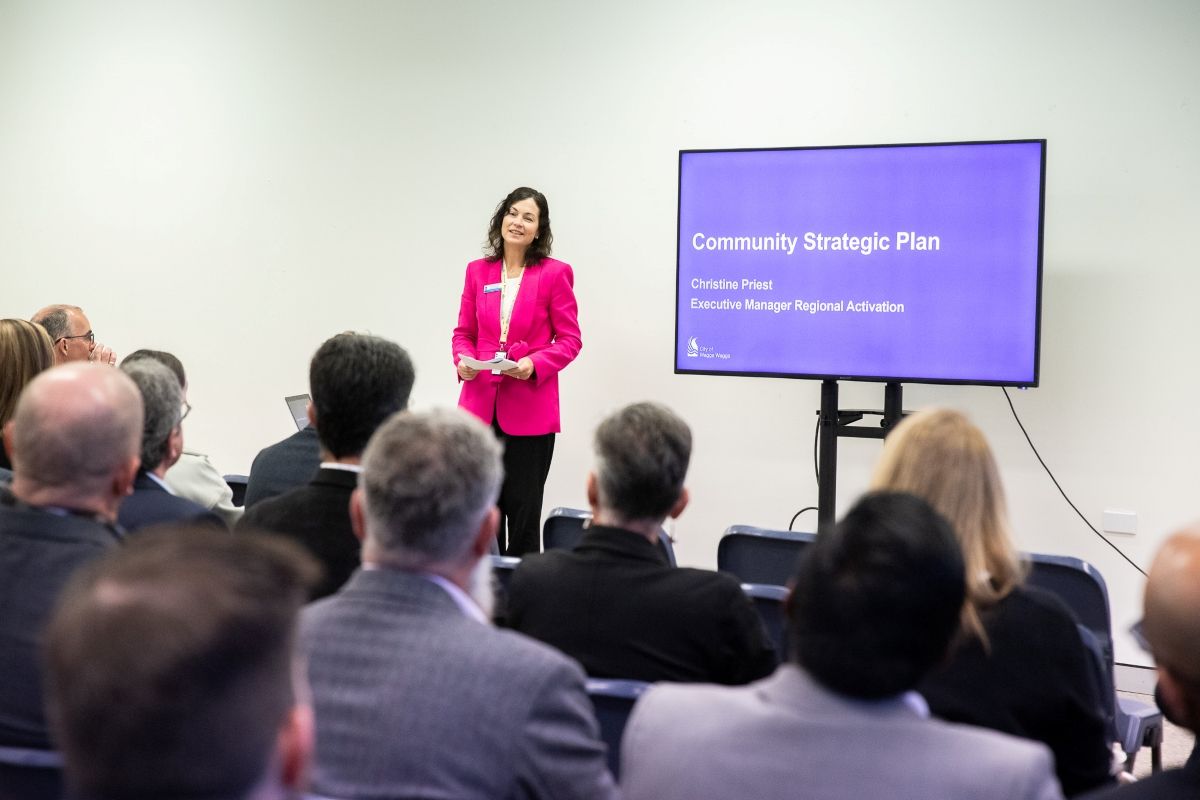 A woman stands in a room addressing a crowd of people.