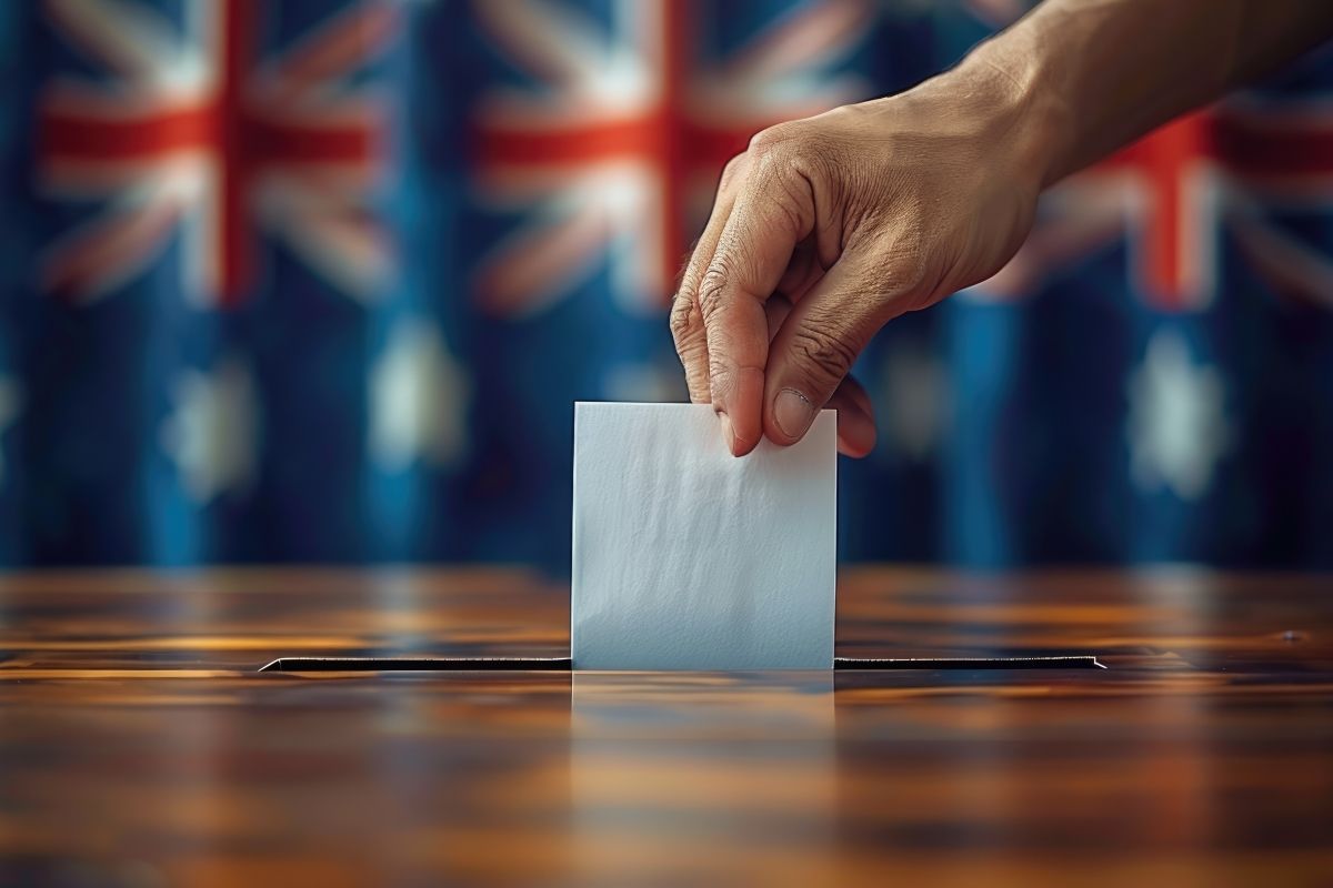 Hand holding ballot paper putting it into ballot box, with Australian flag in background