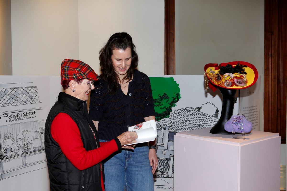 Two women looking at a small book. The older of the two women is holding the book open in her hands.